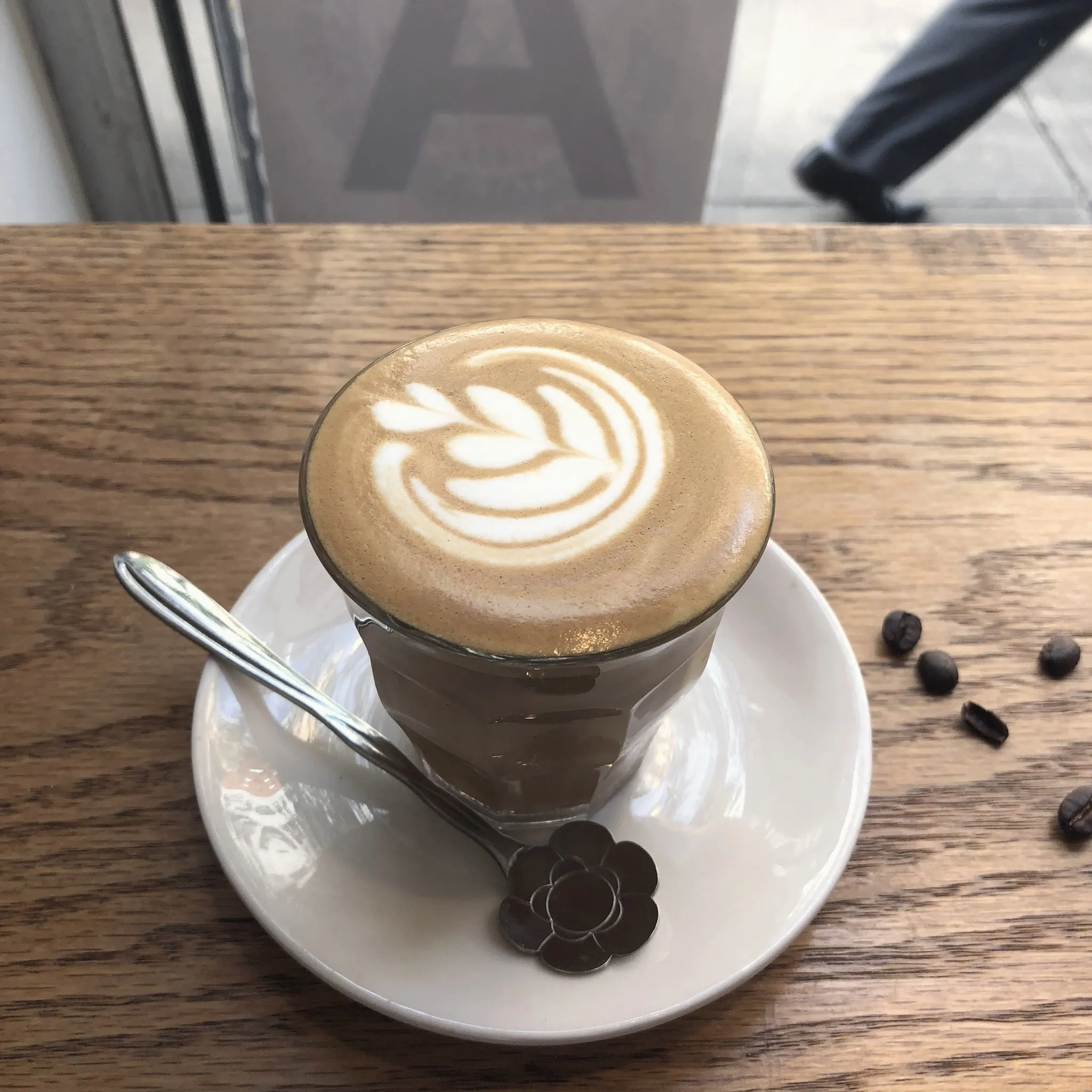 A flat white with tulip latte art on a wooden cafe counter